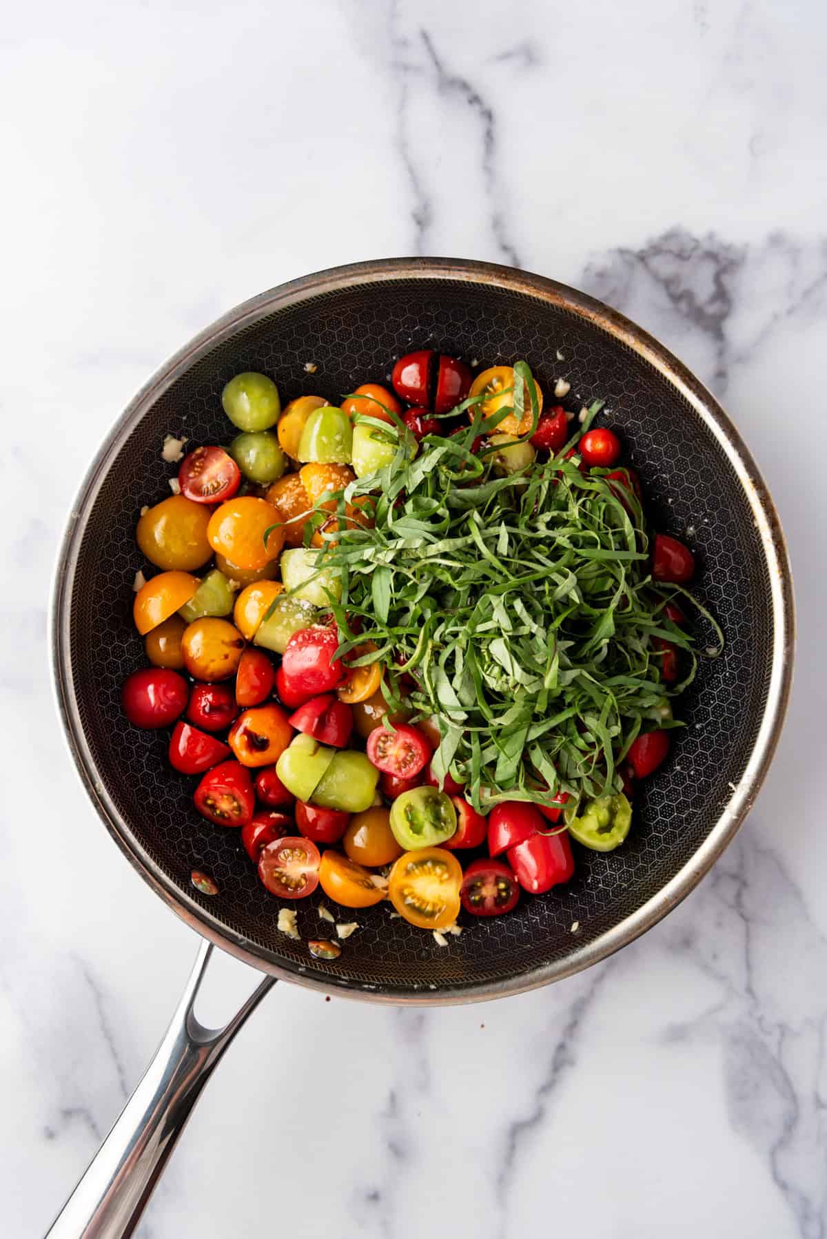 Adding thinly sliced fresh basil to tomatoes in a pan.