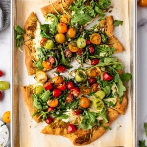 A four cheese pizza topped with tomatoes, basil, and arugula with slices pulled away.