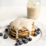 A stack of homemade lemon ricotta pancakes with coconut syrup on a plate.