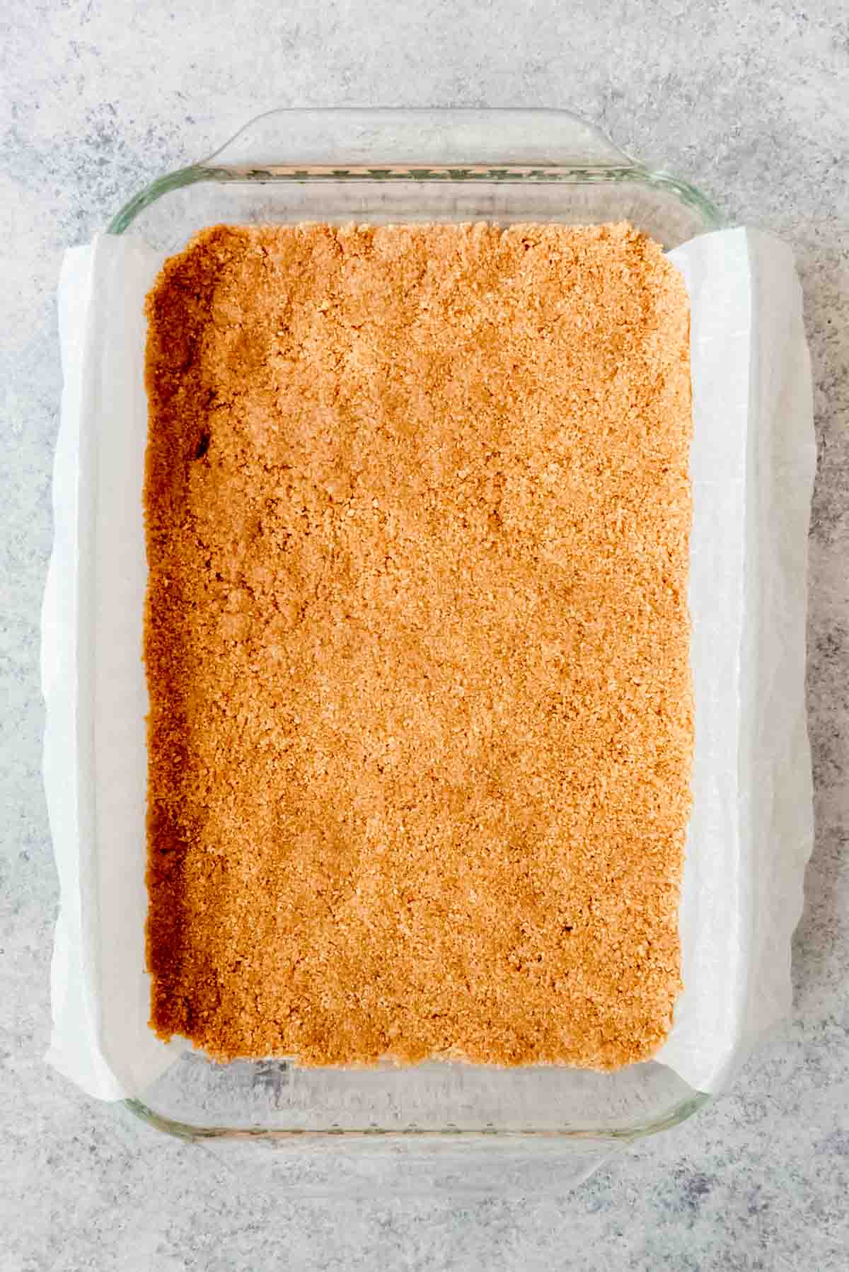 An image off a graham cracker crust in a 9x13-inch glass baking dish.