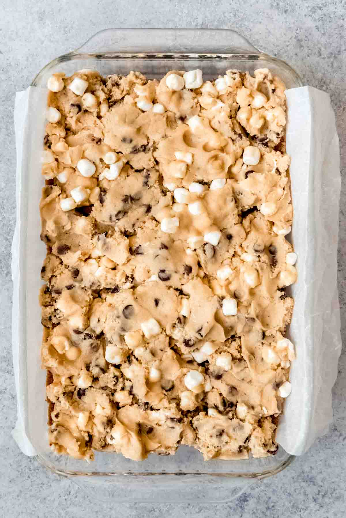 An image of chocolate chip cookie dough pressed into a 9x13-inch baking dish on a graham cracker crust.