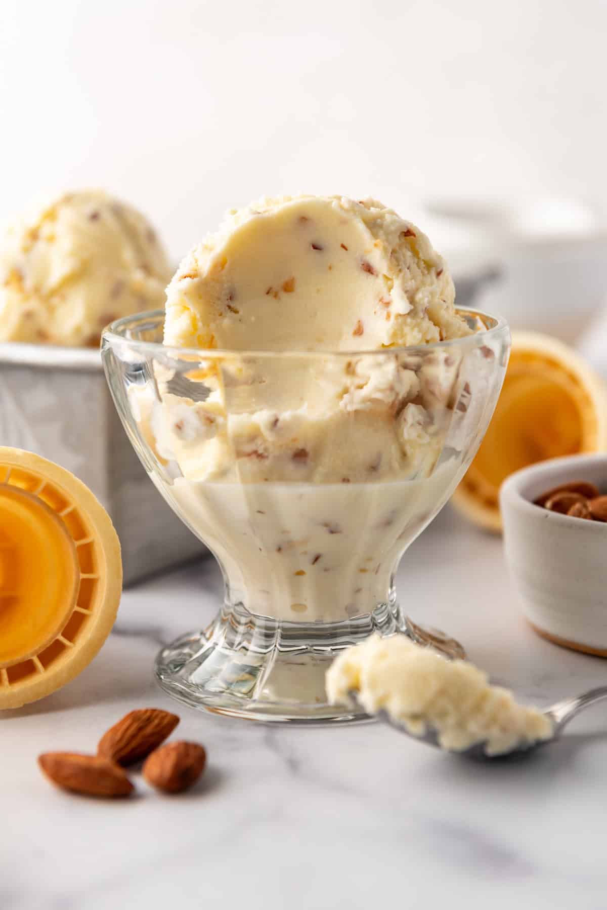 A glass ice cream dish with scoops of toasted almond ice cream.