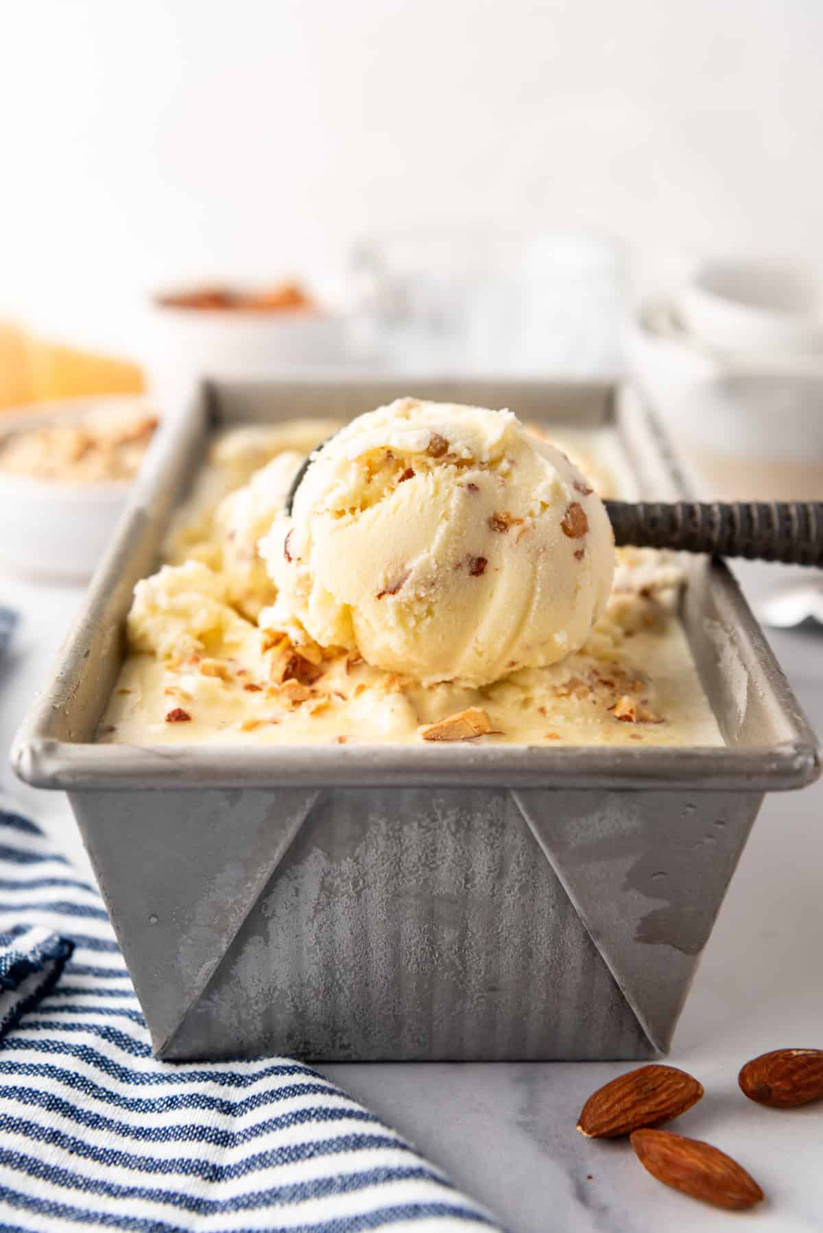 Toasted almond ice cream being scooped out of a pan with an ice cream scoop.