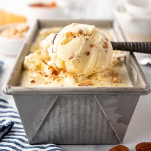 Toasted almond ice cream being scooped out of a pan with an ice cream scoop.