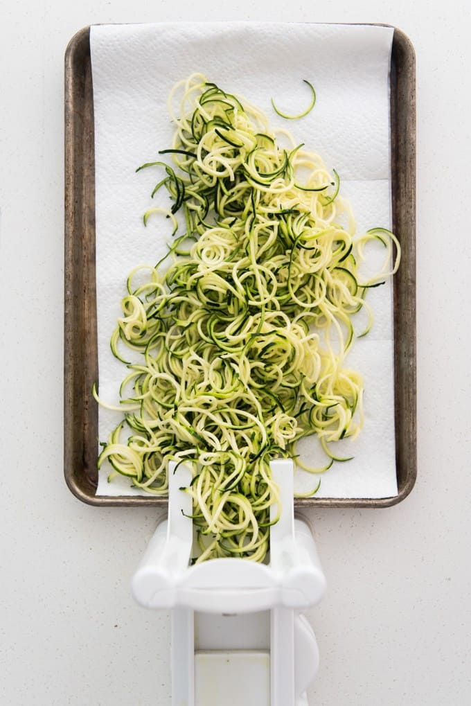 A large pile of spiralized zucchini noodles on a baking sheet lined with paper towels.