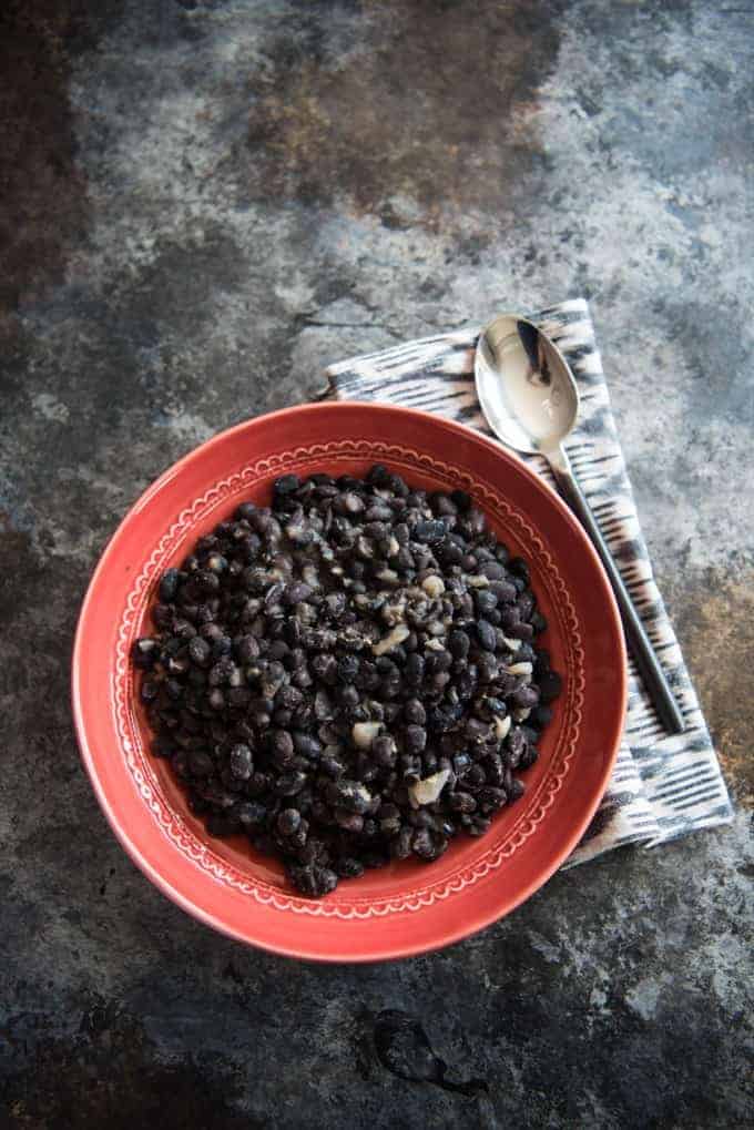 Brazilian black beans with garlic and onions in an orange bowl.