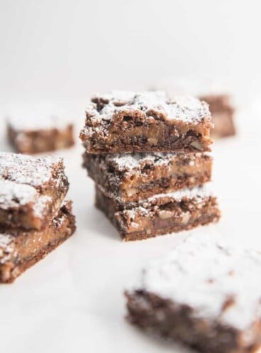 Caramel pecan brownies stacked on top of each other and dusted with powdered sugar.