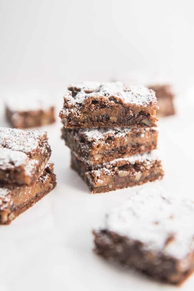 Caramel pecan brownies stacked on top of each other and dusted with powdered sugar.