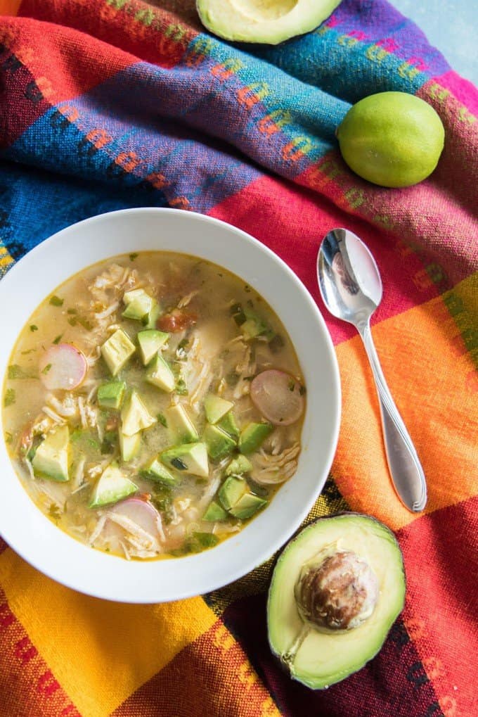 A bowl of a chicken avocado lime soup with radishes on a bright Mexican tablecloth.