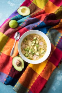 A bowl of chicken avocado lime soup on a brightly colored Mexican tablecloth.