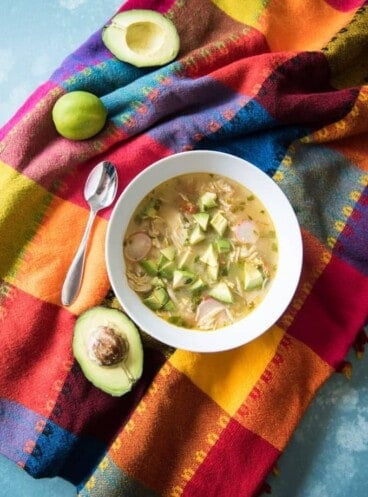 A bowl of chicken avocado lime soup on a brightly colored Mexican tablecloth.