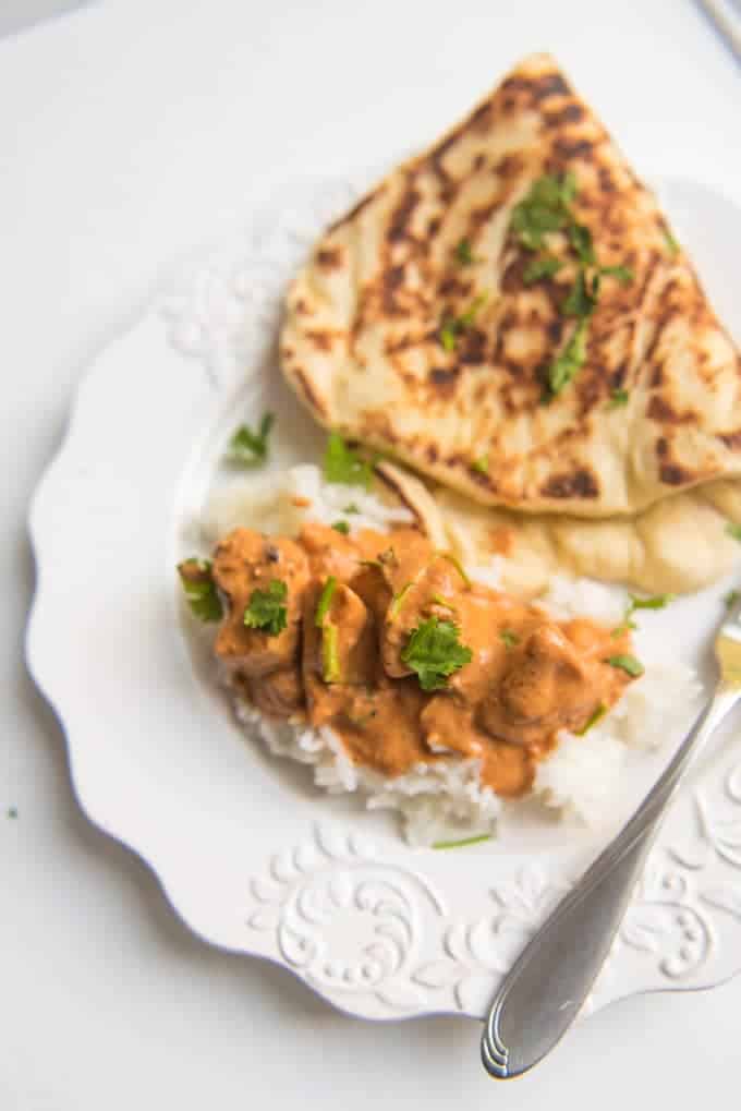 A plate of chicken tikka masala with rice and a piece of garlic naan bread.