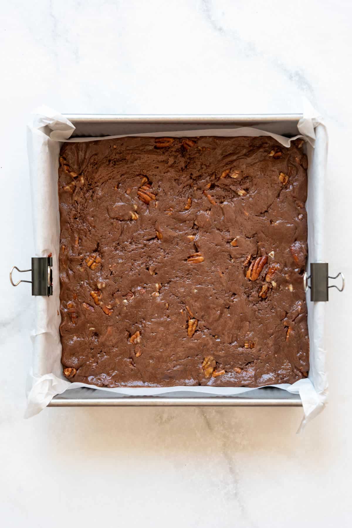 Unbaked brownie batter in the bottom of a square pan.
