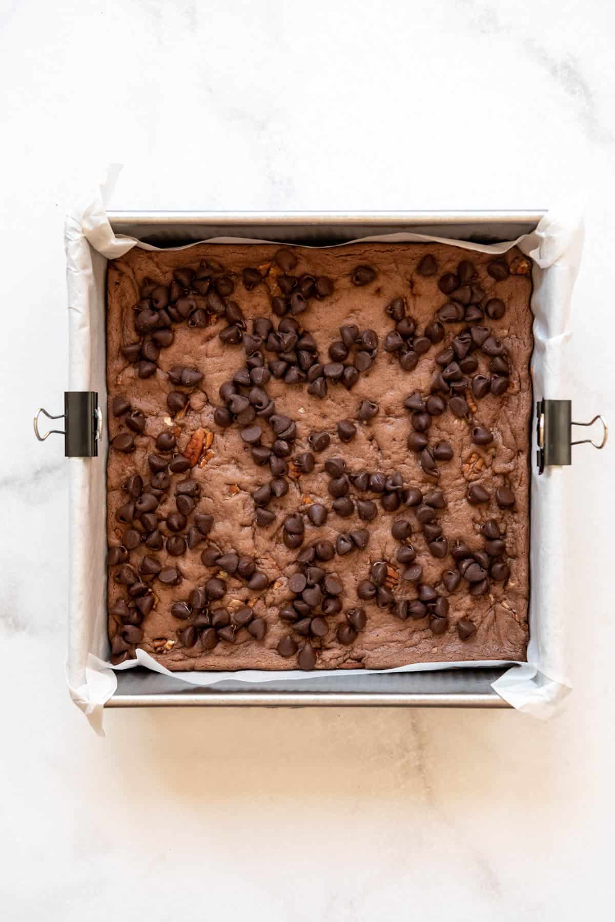 Chocolate chips sprinkled over partially cooked brownies in a square pan.