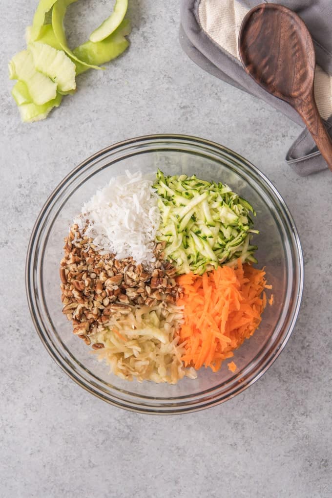 Clockwise from the top are shredded zucchini, shredded carrots, shredded apple, chopped pecans, and shredded coconut for making morning glory muffins.