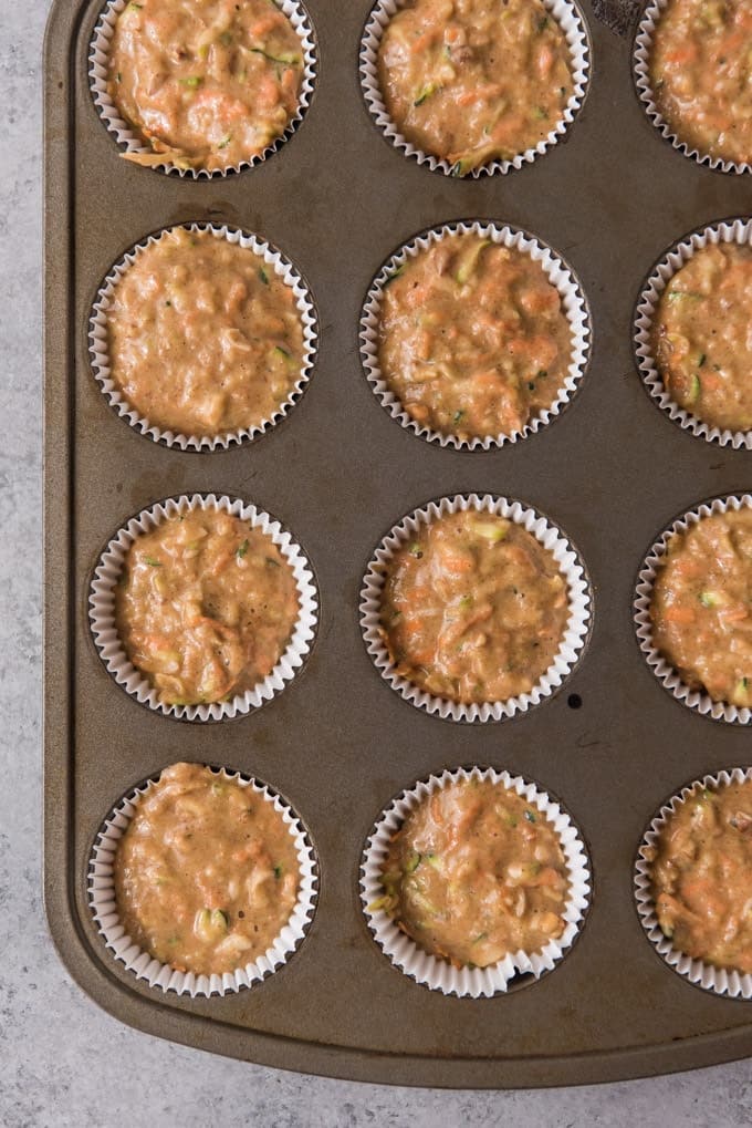 An image of healthy morning glory muffin batter in cupcake liners in a muffin pan.
