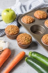 Morning glory muffins with carrots, zucchini and apple next to them.