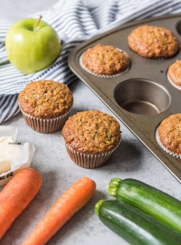 Morning glory muffins with carrots, zucchini and apple next to them.