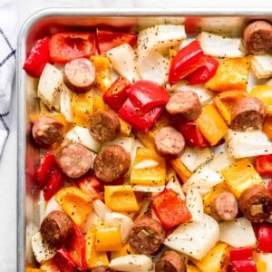 A square image of chicken sausage, colorful bell peppers, and onions on a sheet pan.