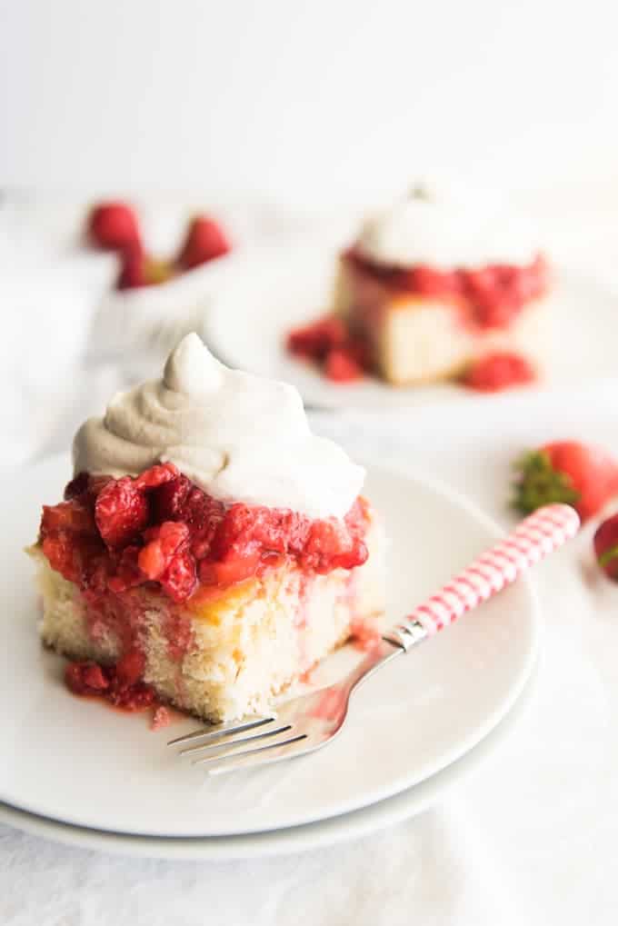 A slice of white cake topped with macerated strawberries and whipped cream.