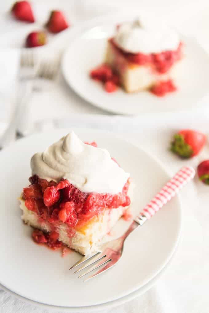 Mashed strawberries and freshly whipped cream piled on top of slices of white cake on white plates.