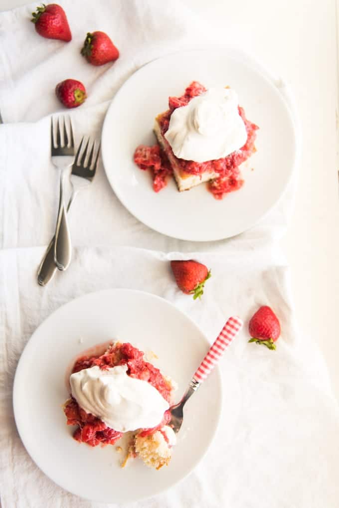 Two slices of strawberry shortcake on white plates next to some forks.