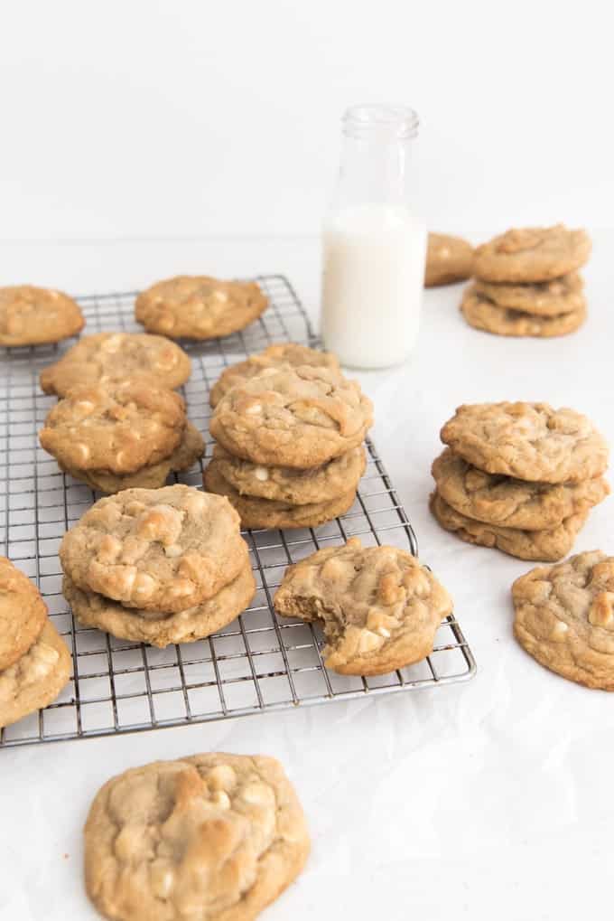 White chocolate macadamia nut cookies on a wire cooling rack with a glass of milk nearby.