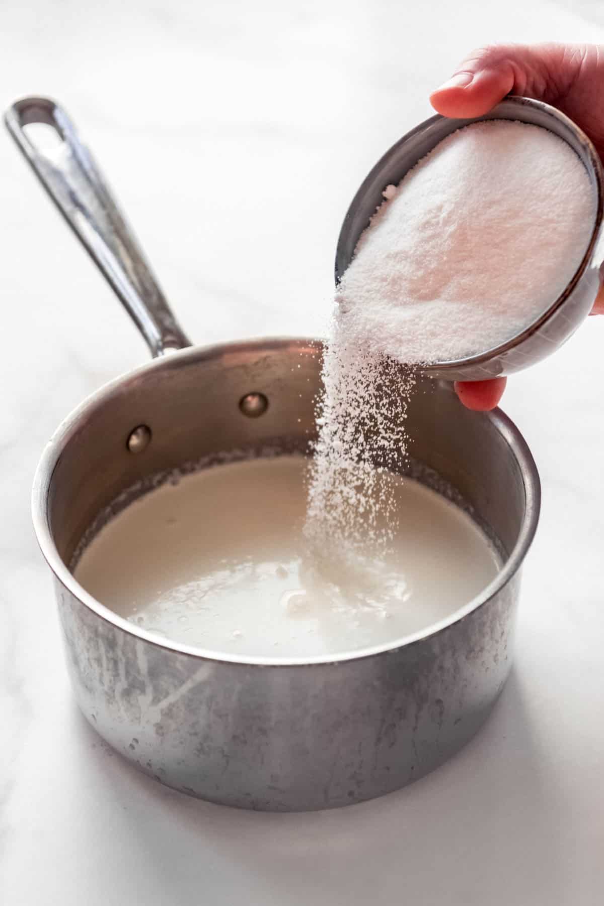 sugar being added to milk and cream in a saucepan