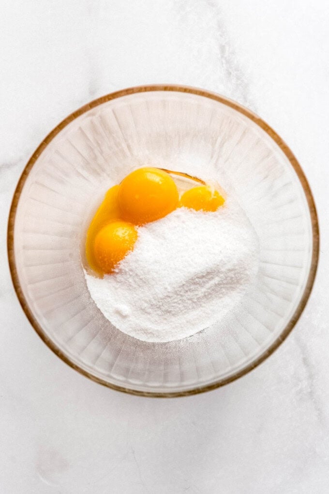 An image of granulated sugar and egg yolks in a glass bowl.