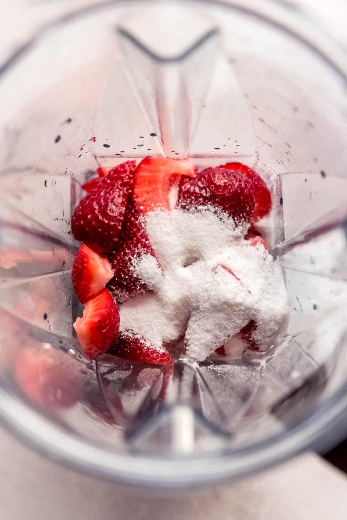 Combining strawberries and sugar in a blender.