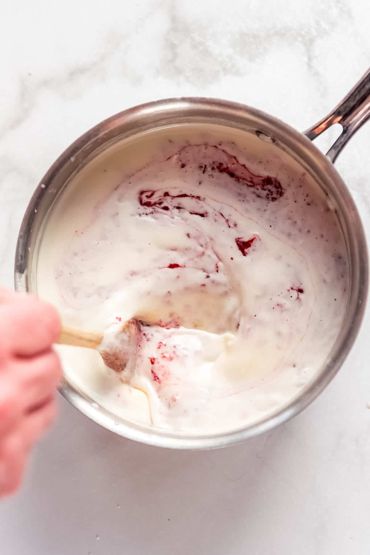 A wooden spoon stirring strawberry puree into a custard ice cream base.