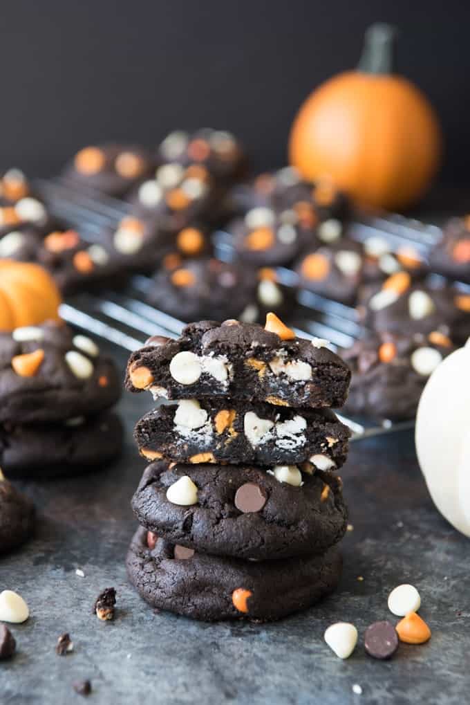a stack of Dark Chocolate Halloween Chip Cookies with more cookies, chocolate chips and pumpkins around it