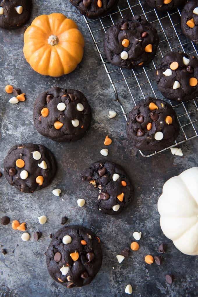 Dark Chocolate Halloween Chip Cookies scattered around on and off of a cooling rack with a cookie in the lower center missing a bite