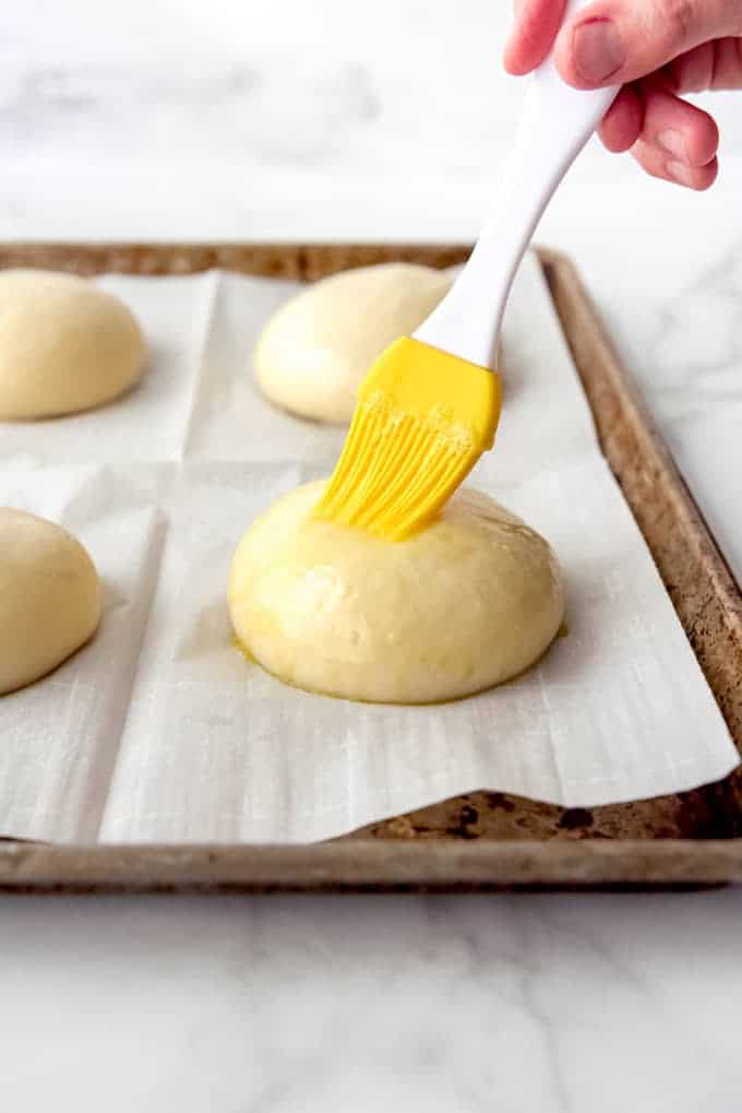 An image of a pastry brushing being used to brush egg wash onto homemade burger buns.