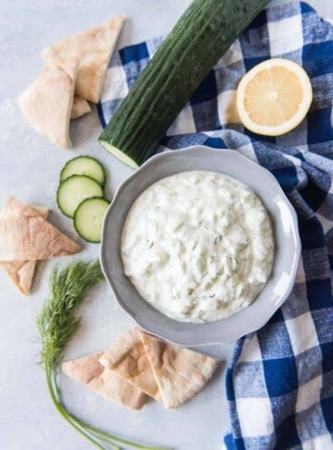 Greek Tzatziki Saucein a bowl surrounded by bread and ingredients