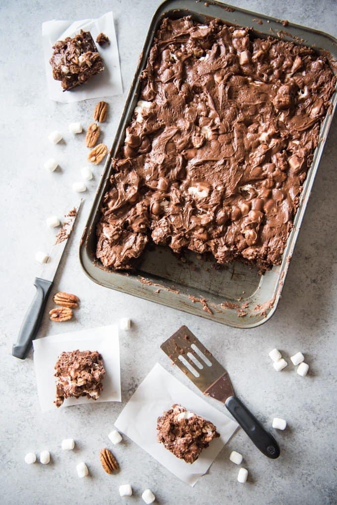 A baking dish filled with Mississippi Mud Brownies and someservings removed with scattered marshmallows and walnuts around it