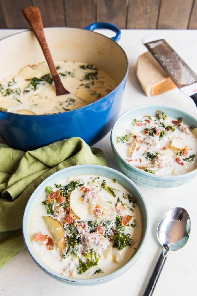 zuppa toscana in a blue pot and in white bowls with cheese and spoon to the side