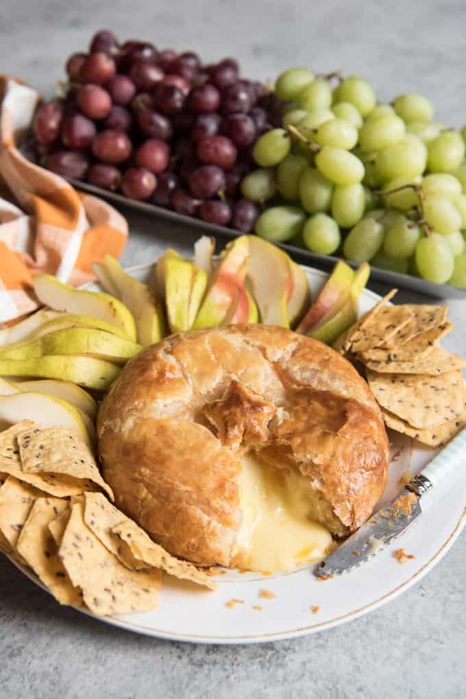 baked brie with puff pastry on a plate with grapes and apple slices
