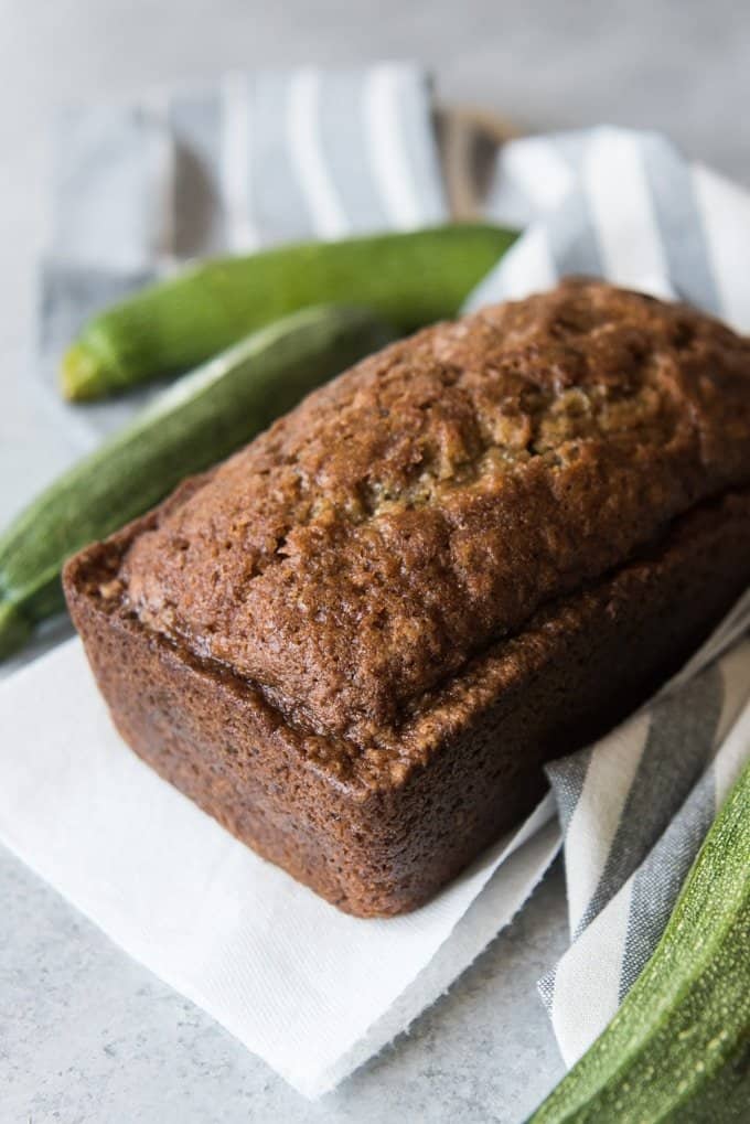 a loaf of zucchini bread with two zucchinis in the background