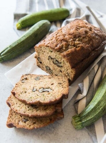 sliced zucchini bread with whole zucchinis next to it