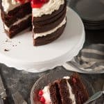 a black forest cake on a cake stand with a slice removed and placed on a plate below
