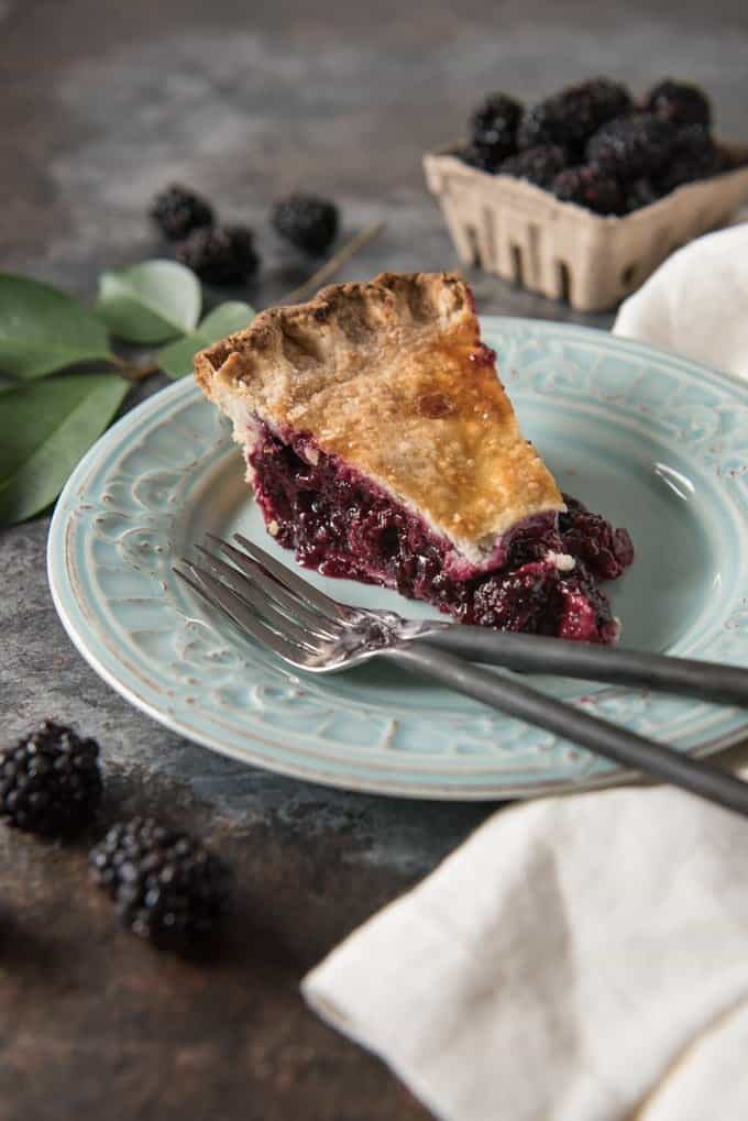 Close up of a slice of blackberry pie on a light blue plate with a fork.