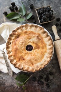 an aerial view of a baked blackberry pie next to a rolling pin and fresh blackberries