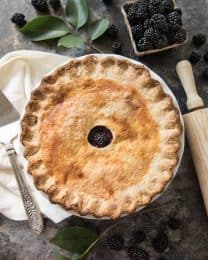 an aerial view of a baked blackberry pie next to a rolling pin and fresh blackberries