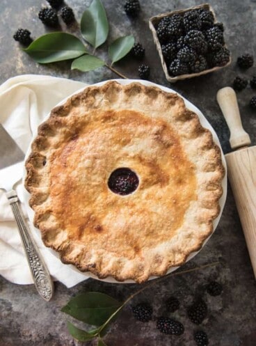 an aerial view of a baked blackberry pie next to a rolling pin and fresh blackberries