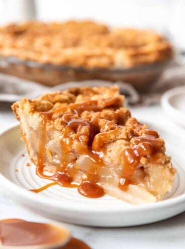 Caramel sauce on top of a slice of dutch pear pie on a plate with more pie in the background.