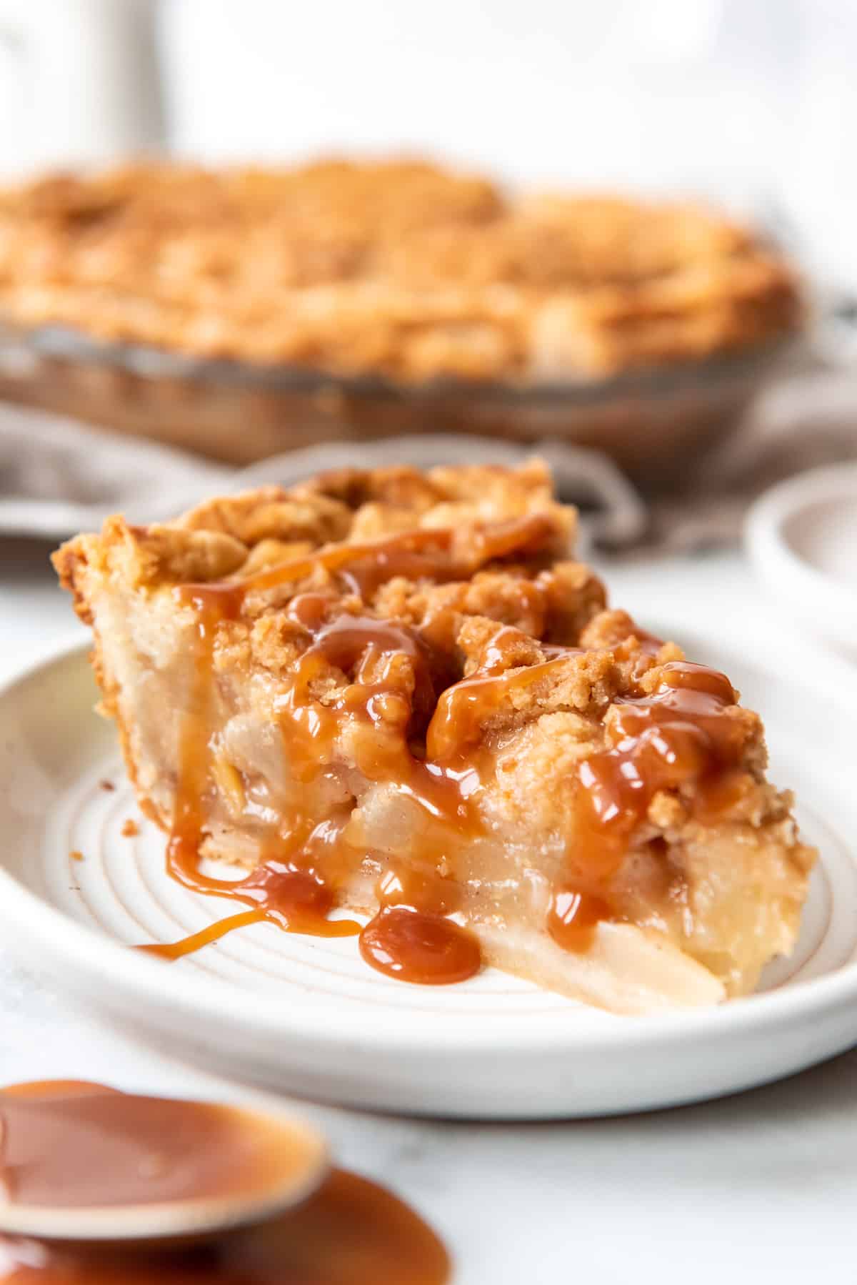 Caramel sauce on top of a slice of dutch pear pie on a plate with more pie in the background.