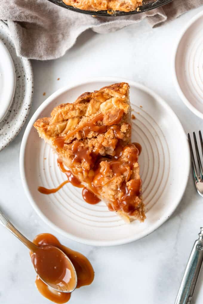 A single slice of pear pie drizzled with homemade caramel sauce on a white plate.