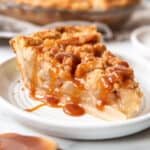 A slice of homemade pear pie with crumb topping and salted caramel sauce drizzled on top.