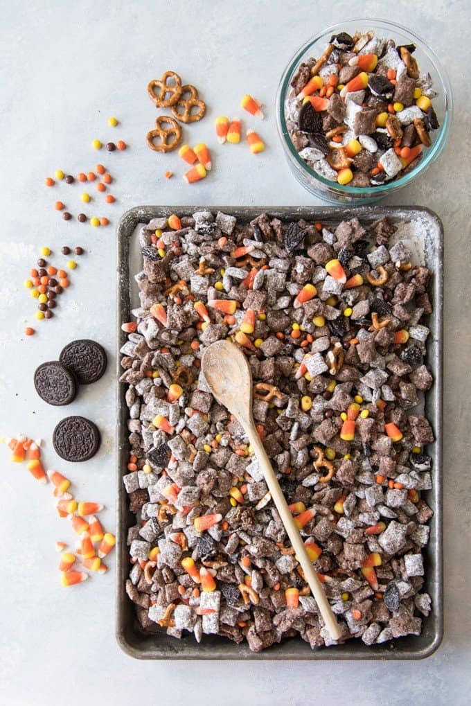 halloween chex mix muddy buddies on a baking sheet with a wooden spoon and in a bowl to the side